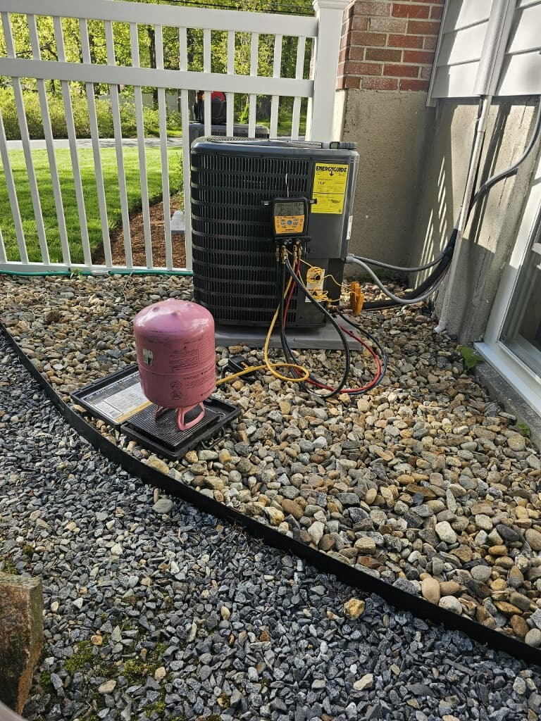 Outdoor air conditioning unit being serviced with a pink refrigerant tank and digital gauges.